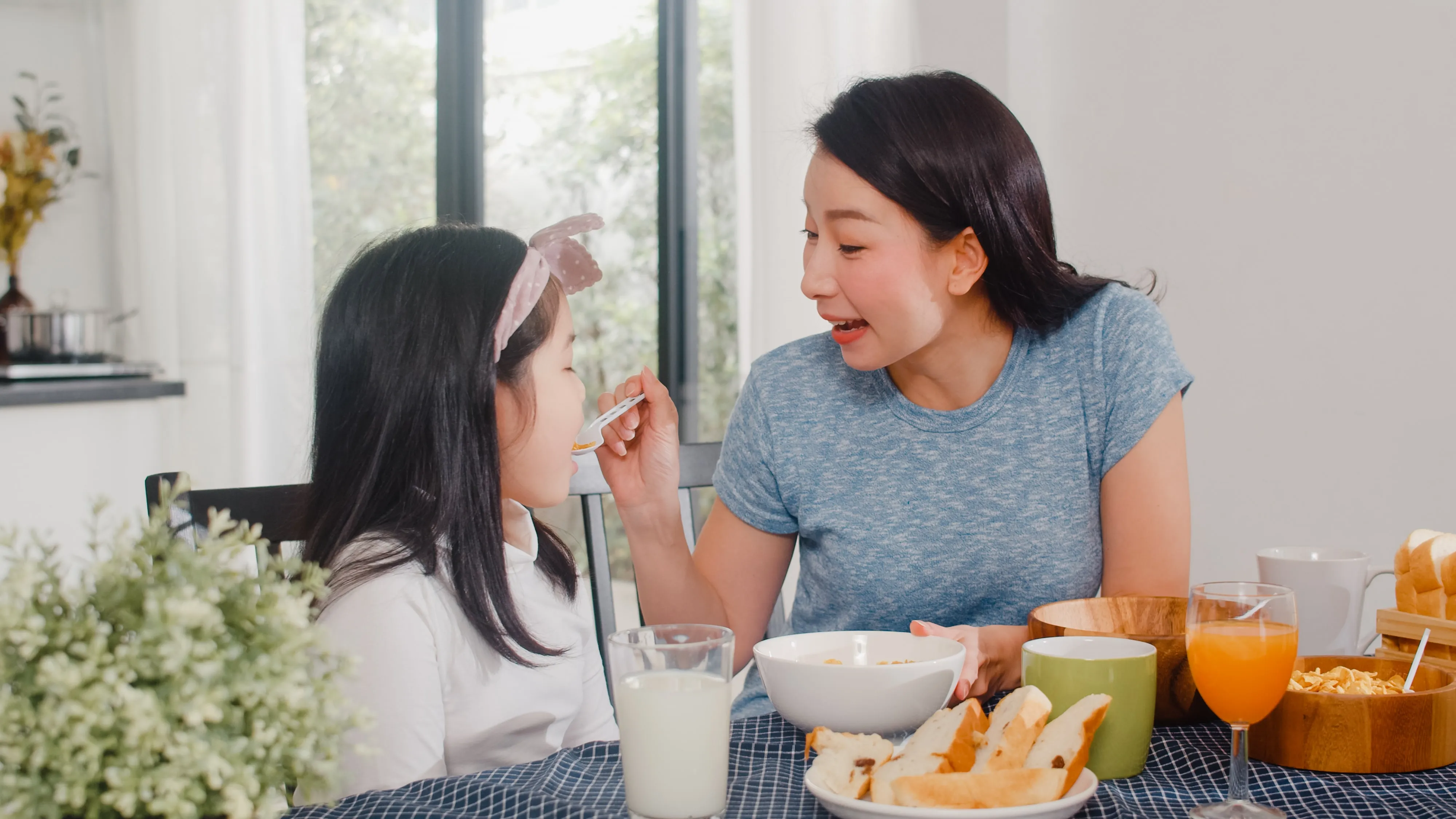 asian japanese family has breakfast home asian mom daughter happy talking together while eating bread drink orange juice corn flakes cereal milk table modern kitchen morning lumina homes