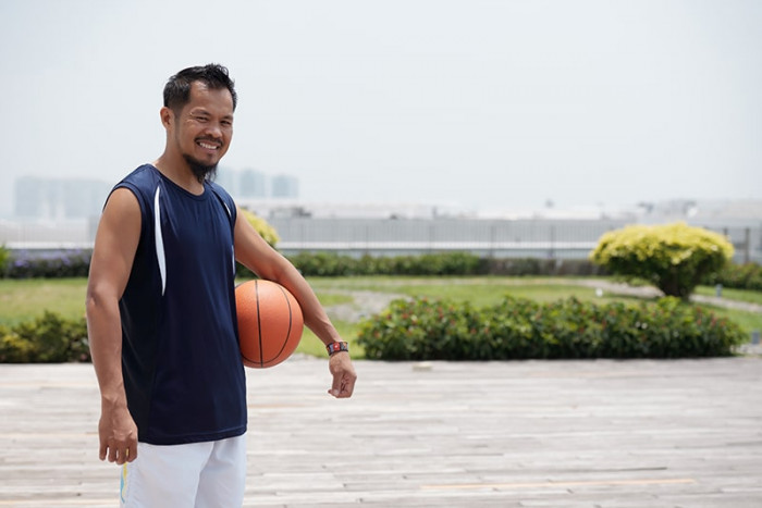 asian man standing outdoors stadium holding basketball smiling min