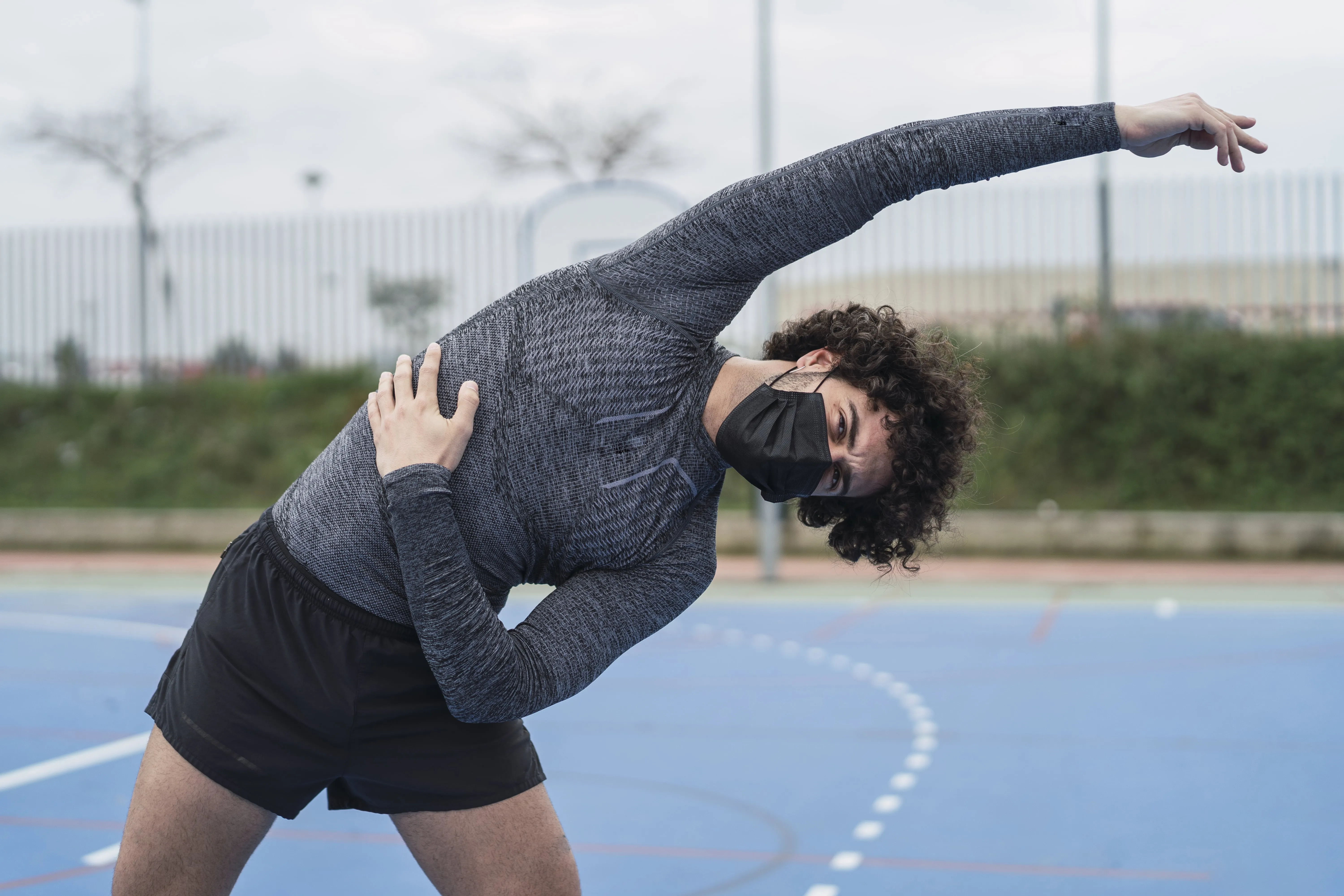 young spanish male wearing black mask is doing stretching exercise min