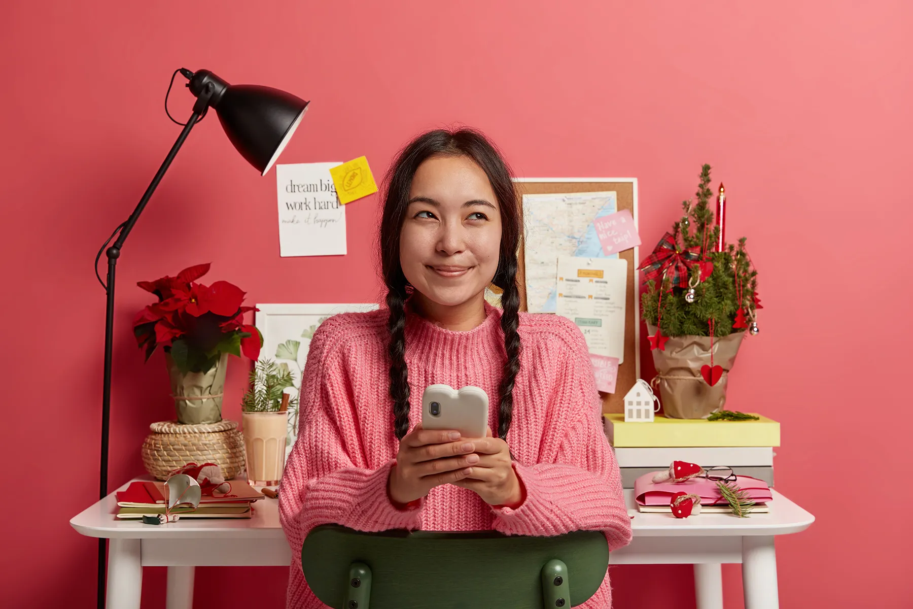 dreamy cheerful millennial girl sits relaxed against desktop chats with friends has work break sending message decorates workplace christmas